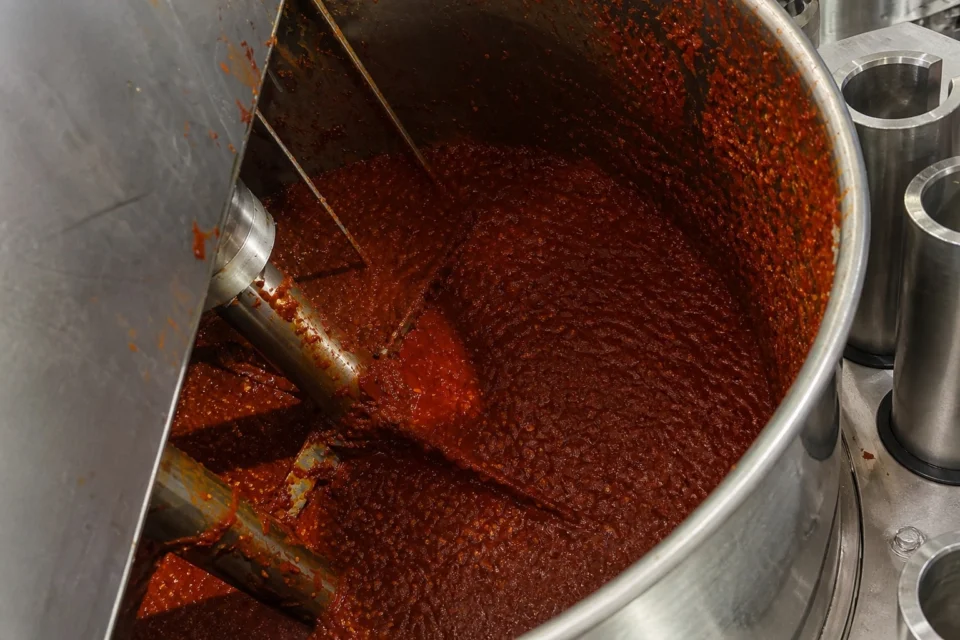 Thick chili sauce with visible seeds and particles inside a filling-machine hopper